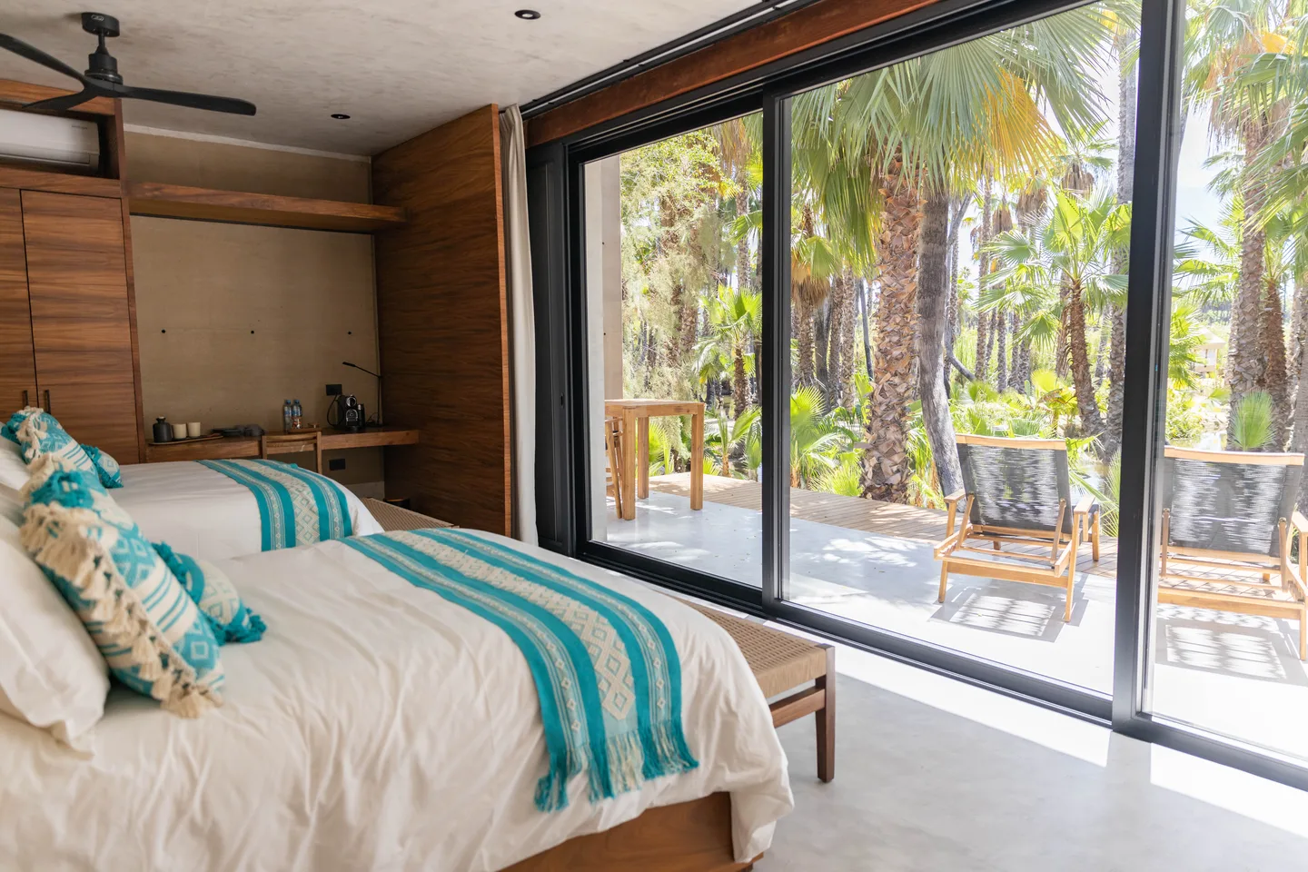 Bed with turquoise woven cushions beside full-height glass doors to the private terrace, Terra Double Room at NEST Los Cabos