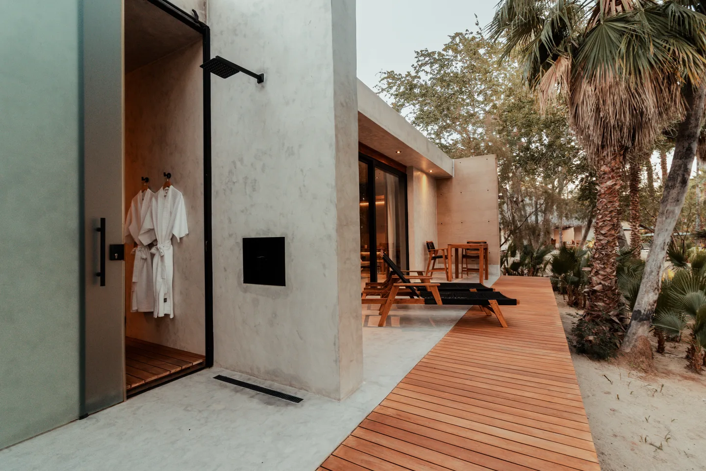 Outdoor shower with bathrobes and a timber walkway to the terrace of a Terra room at NEST Los Cabos